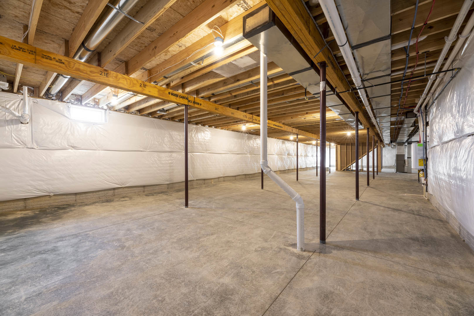 Exposed white pipes running along unfinished basement ceiling, concrete floor, steel beams, and bare walls