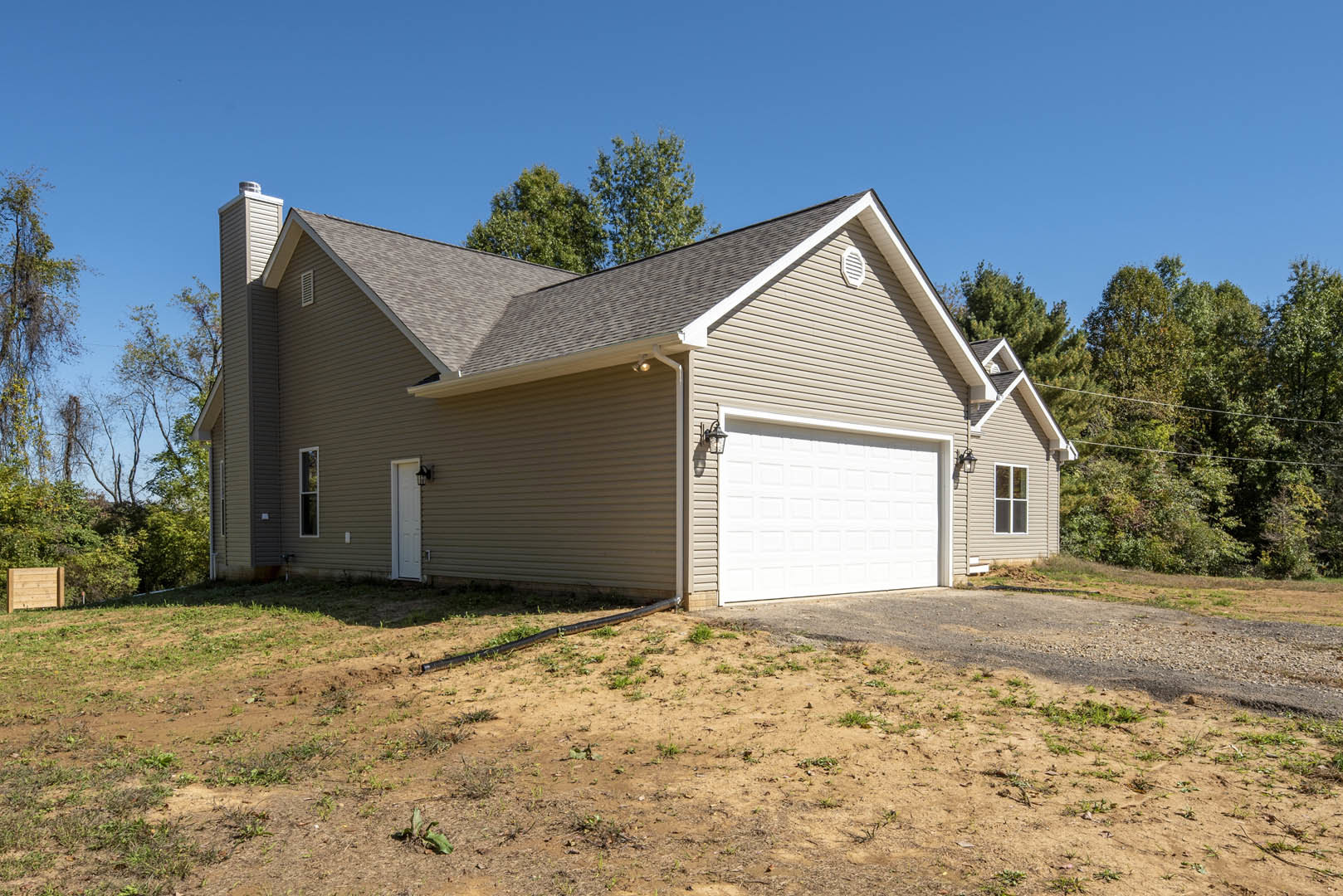 Modern home with attached garage, white siding, wooden fence bordering green lawn, concrete driveway, black drainage pipe near garage, small snake on dirt patch