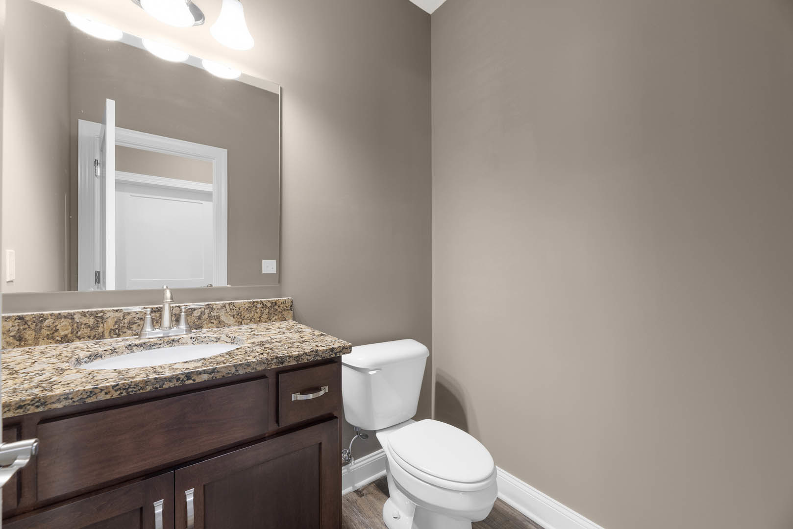 Bathroom with marble countertop vanity, undermount sink, white toilet, light tile flooring, and white door partially open to wall