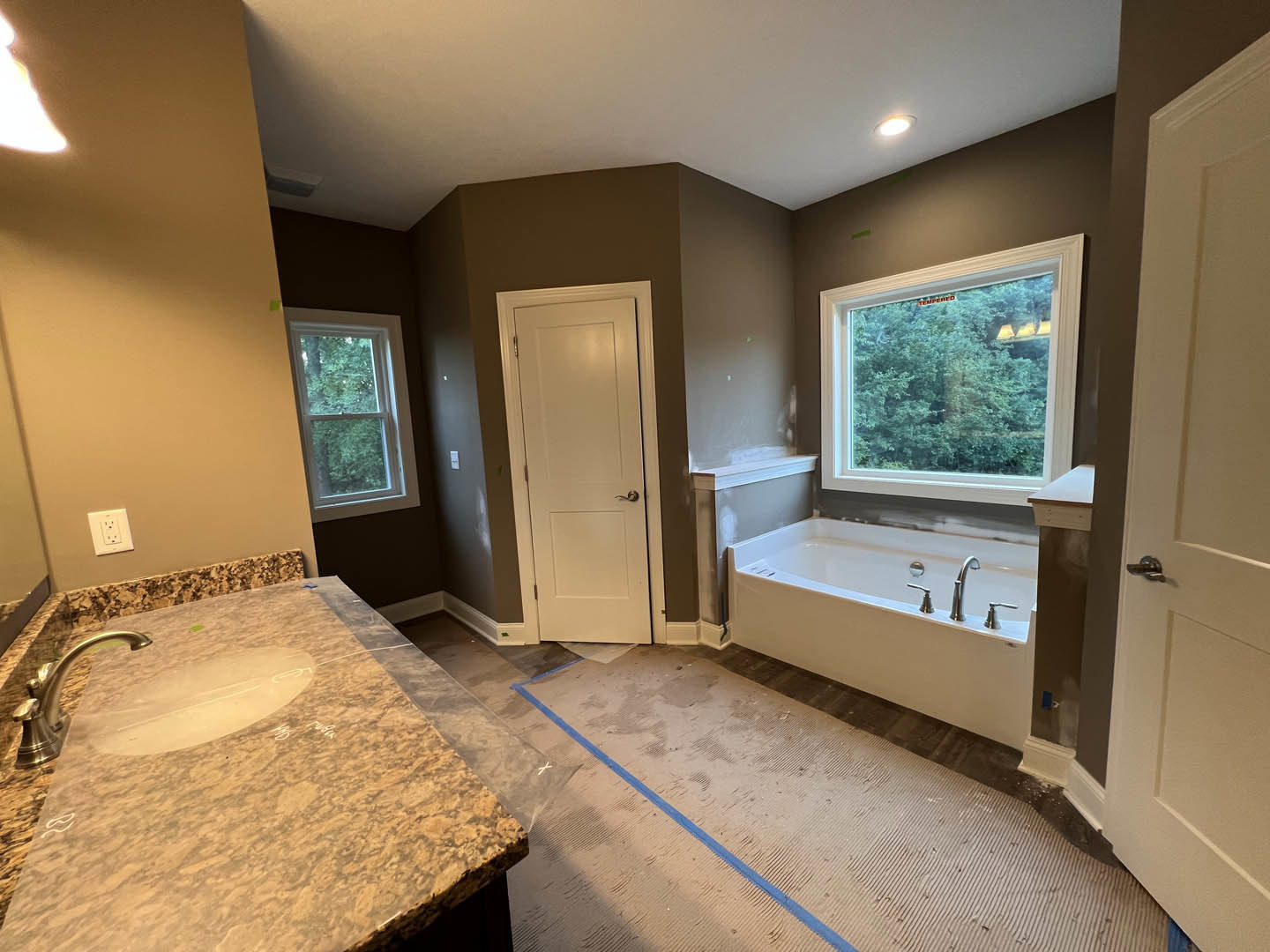 Marble countertop with undermount sink and chrome faucet, freestanding bathtub near window overlooking trees, white door with silver handle, white electrical outlet on wall, light