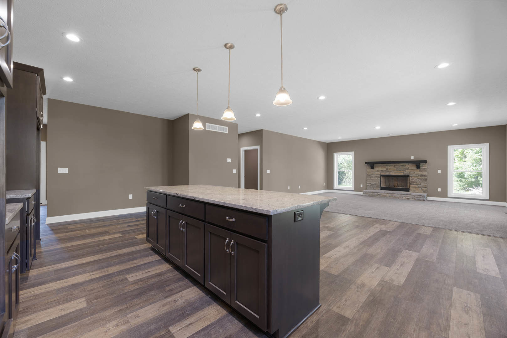 Marble-topped kitchen island with built-in sink and cabinetry, pendant lights hanging from ceiling, tile flooring, fireplace with glass window, large windows revealing trees