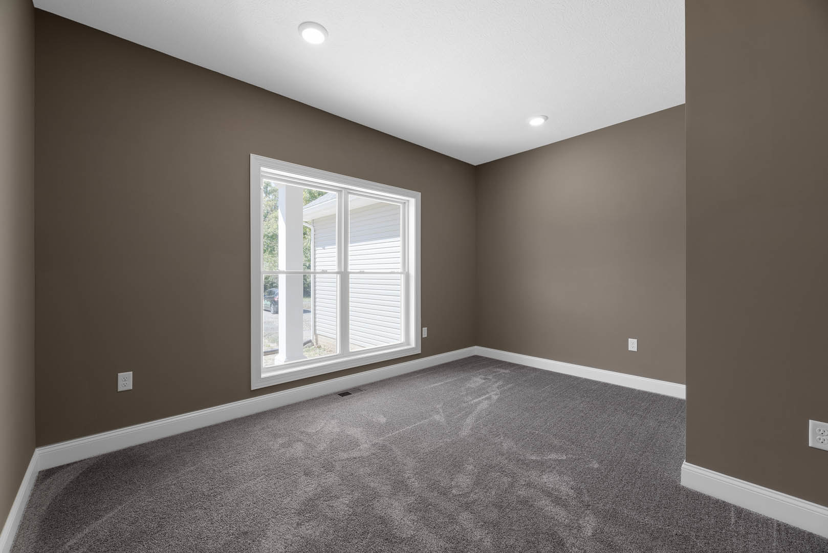 Bedroom with soft grey carpet, white-framed window, light grey walls, ceiling light fixture, and simple white molding