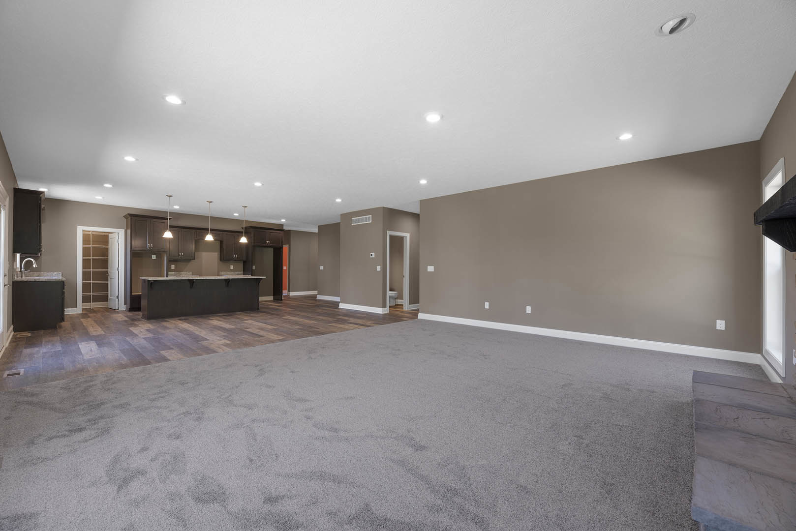 Open-concept kitchen with stone flooring, white ceiling with recessed lights, built-in bar area, and adjacent living space featuring a fireplace and plaster walls