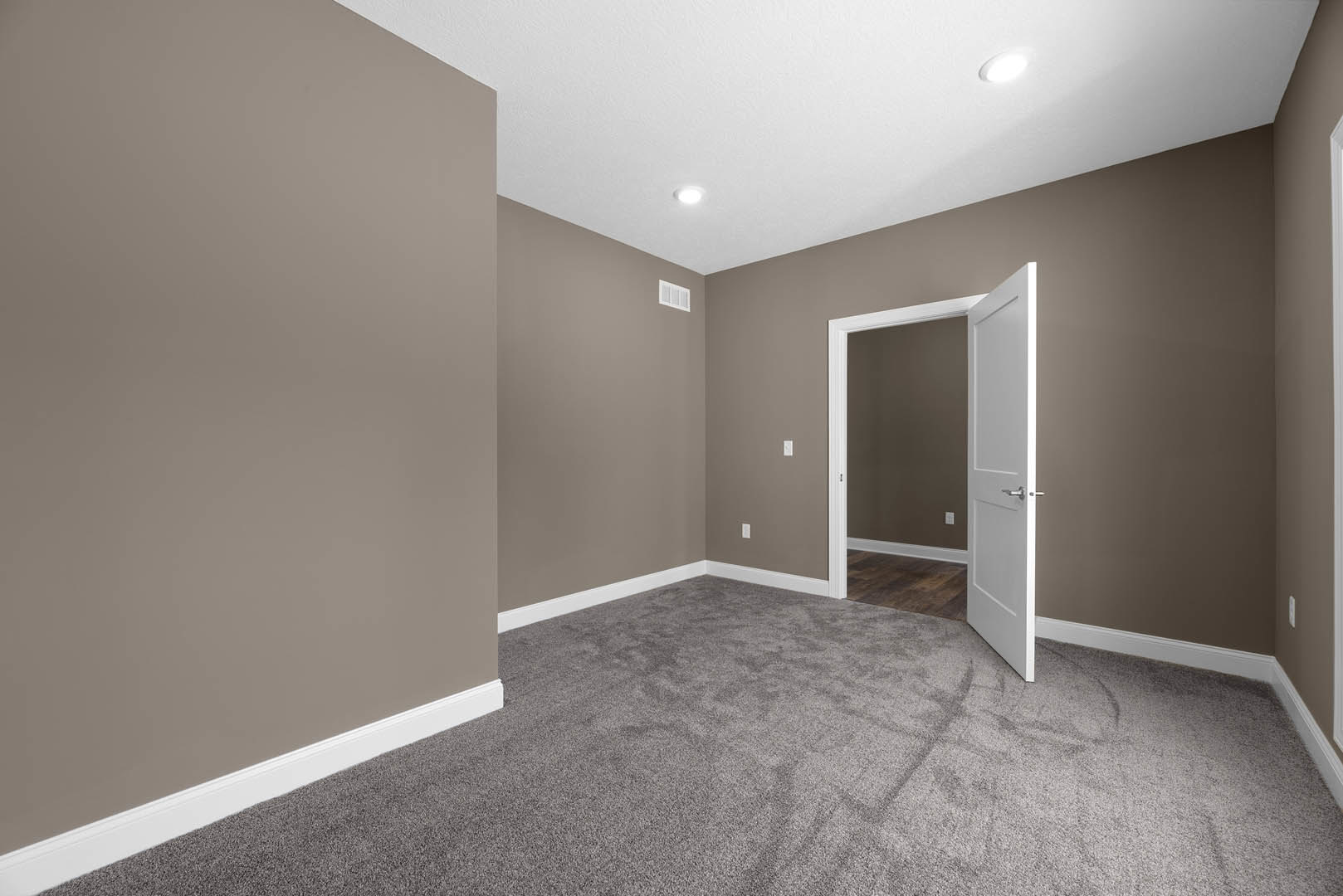 White paneled door with silver handle open to carpeted room, recessed ceiling light, white plaster walls, wood laminate flooring in foreground
