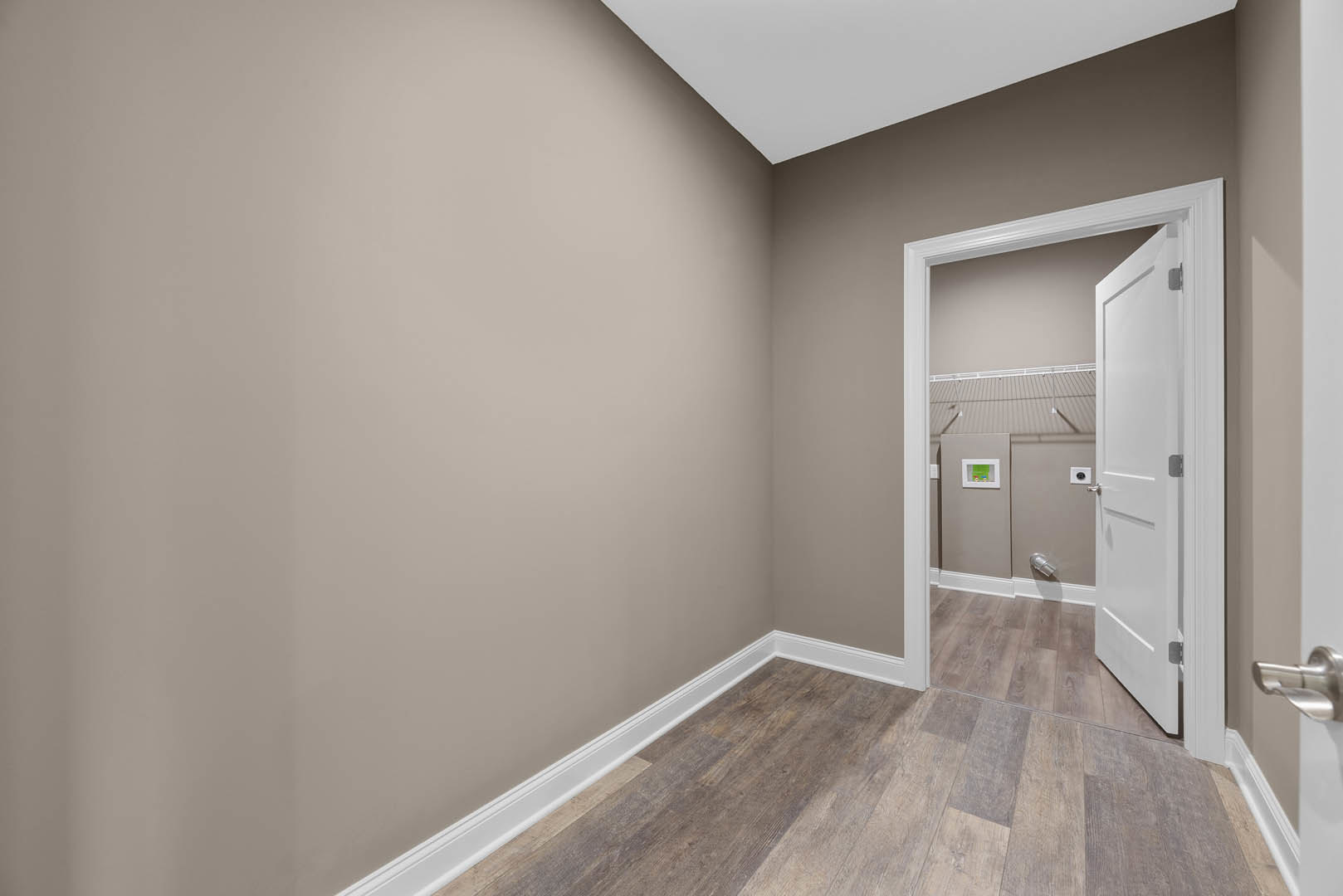 White paneled door with silver handle open to a room featuring wood flooring, white walls, and baseboard trim; closet visible in background.