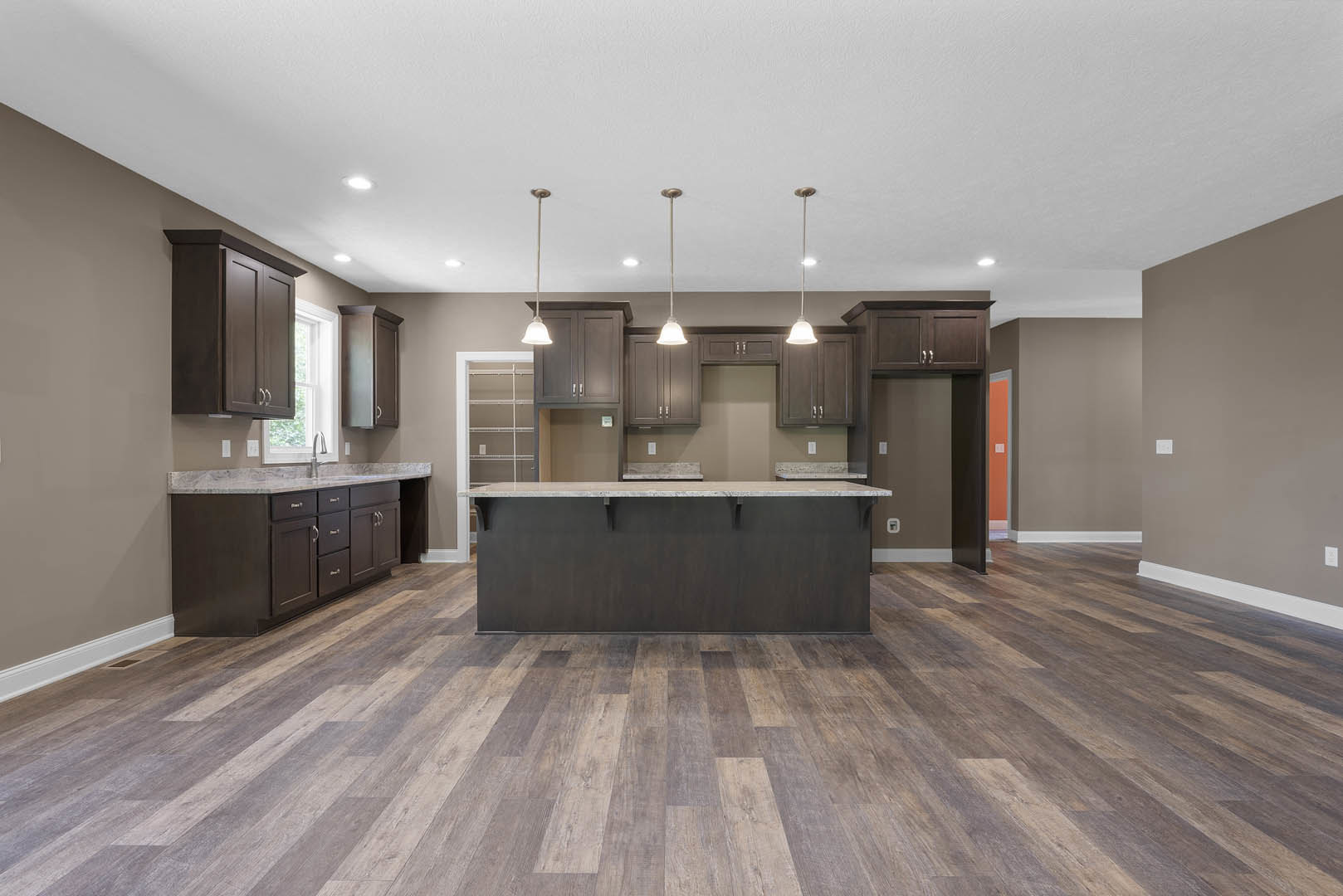 Spacious kitchen featuring a large central island with stone countertop, wood flooring, black accent wall, modern cabinetry, tile backsplash, and recessed ceiling lighting