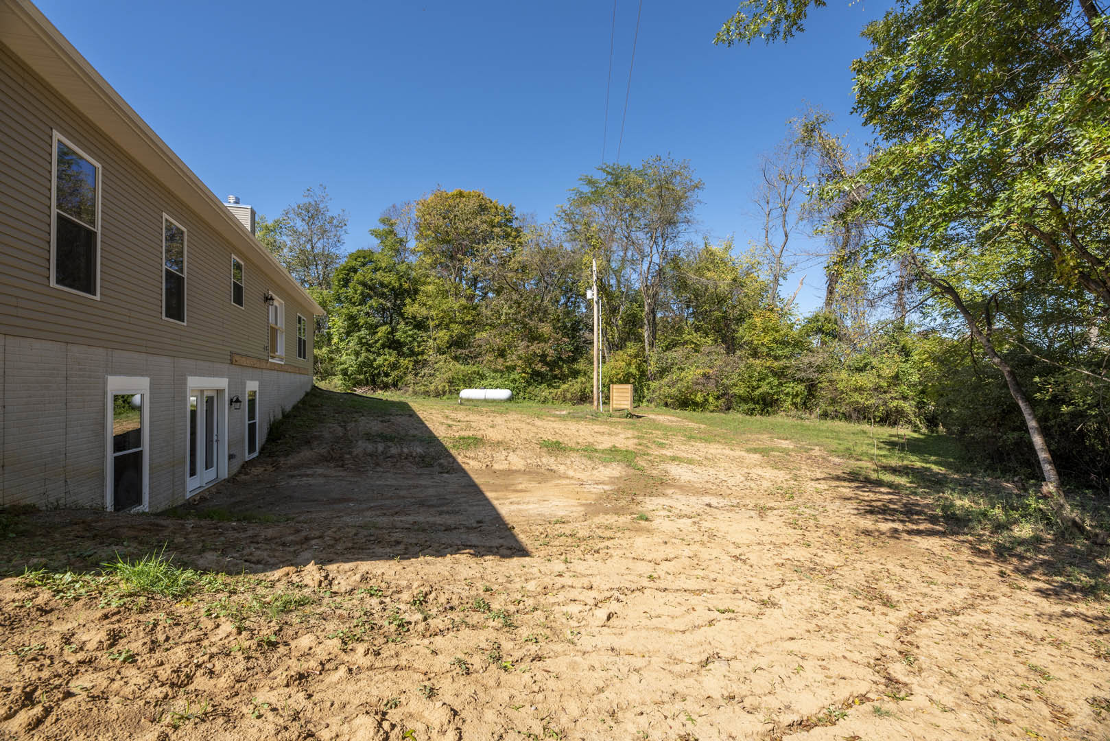 Dirt field beside a modern house with white-framed windows, garage door, and entry door; grassy reflection visible in window, tree and sky in background