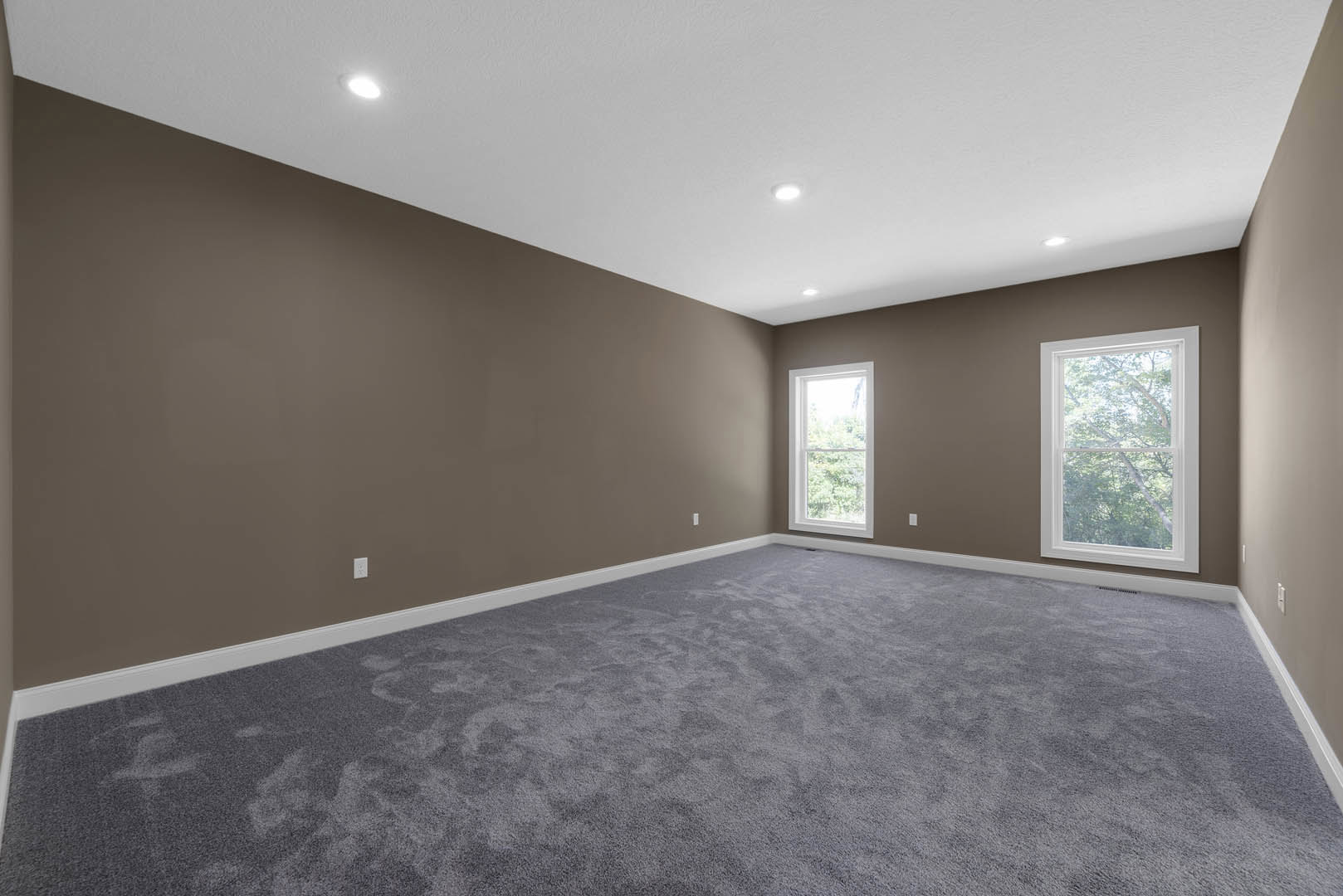 Grey carpeted room with large windows, white ceiling, recessed lighting, and view of trees outside