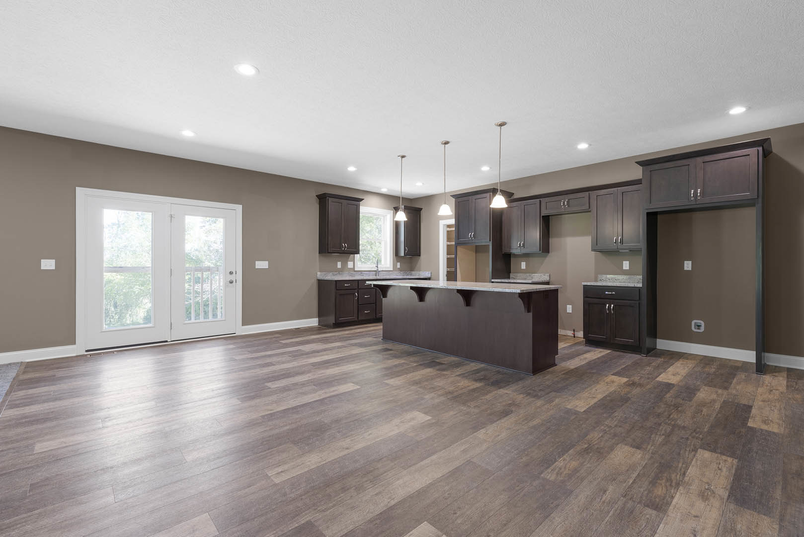 Open kitchen and dining area featuring wood floors, marble countertop, dark brown cabinetry with white top, white double doors with glass panes, and light-colored walls and