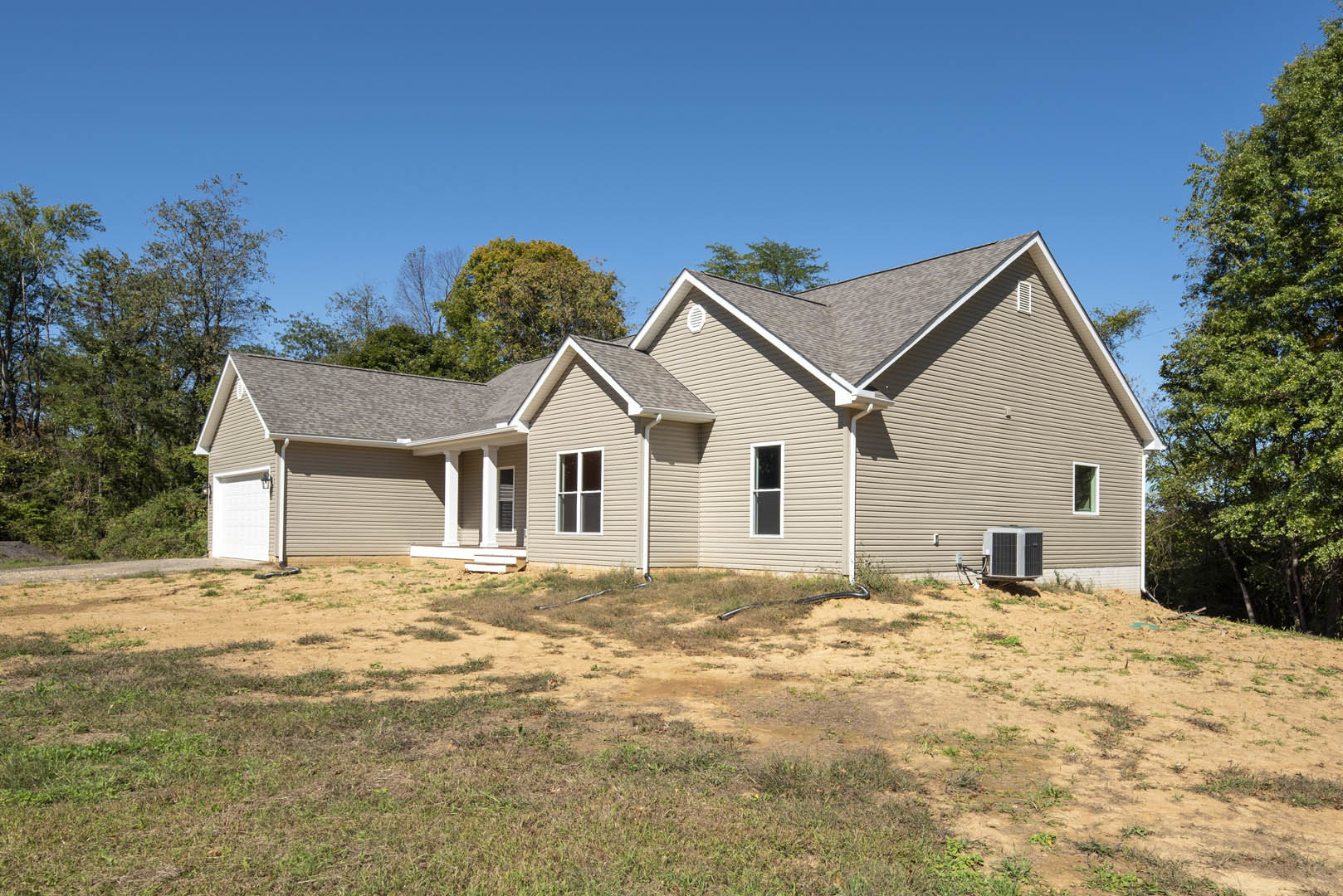 Two-story house with attached garage, parked car in driveway, white-framed windows, green lawn, mature trees, and Robert Frost Farm visible in the background