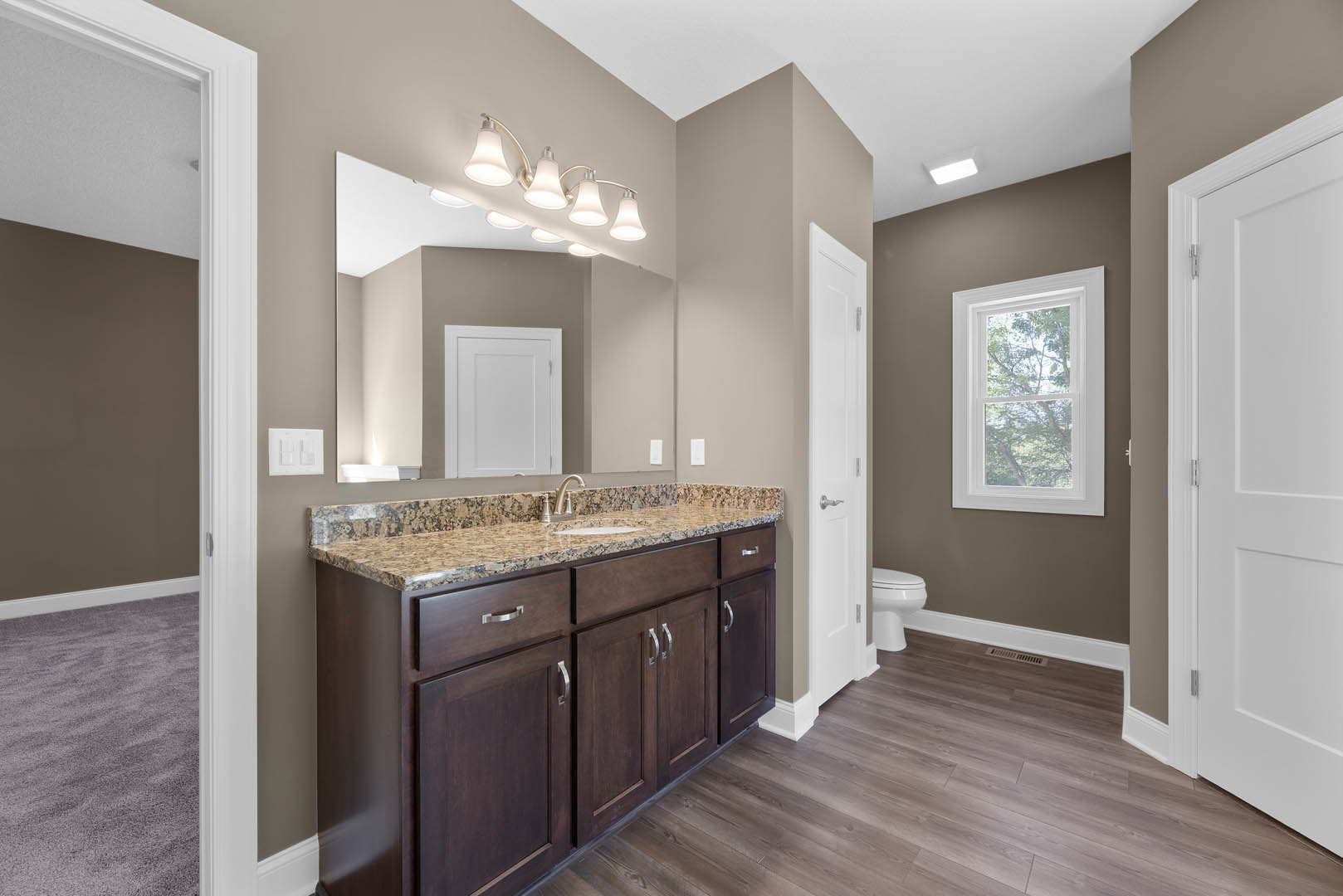 Bathroom featuring a marble countertop, wood flooring, white cabinet, white toilet, ceiling lights, and a window overlooking trees.