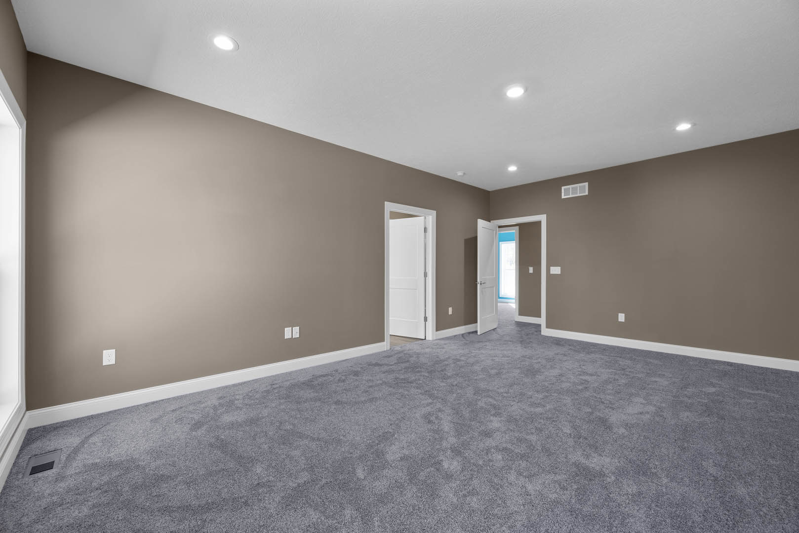 White door with silver handle opens to a room with grey carpet, white walls, wall vent, and ceiling plaster.