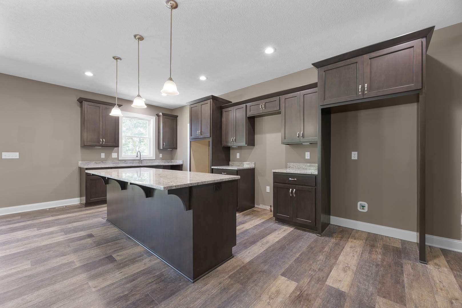 Spacious kitchen featuring a large marble-topped island, wood flooring, white cabinetry, stainless steel fixtures, and a window above the sink.