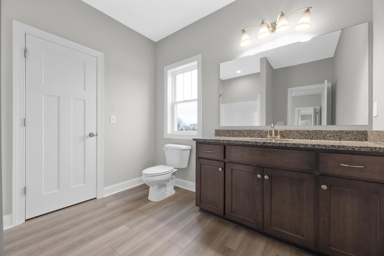 Bathroom with white toilet and rectangular sink, light gray tile flooring, white cabinetry, three-bulb vanity light, white framed window, and white paneled door