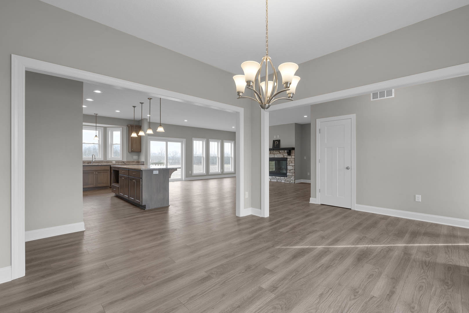 Open kitchen and dining area with marble-topped island, wood flooring, central fireplace, white door with silver knob, and modern chandelier hanging from plaster ceiling