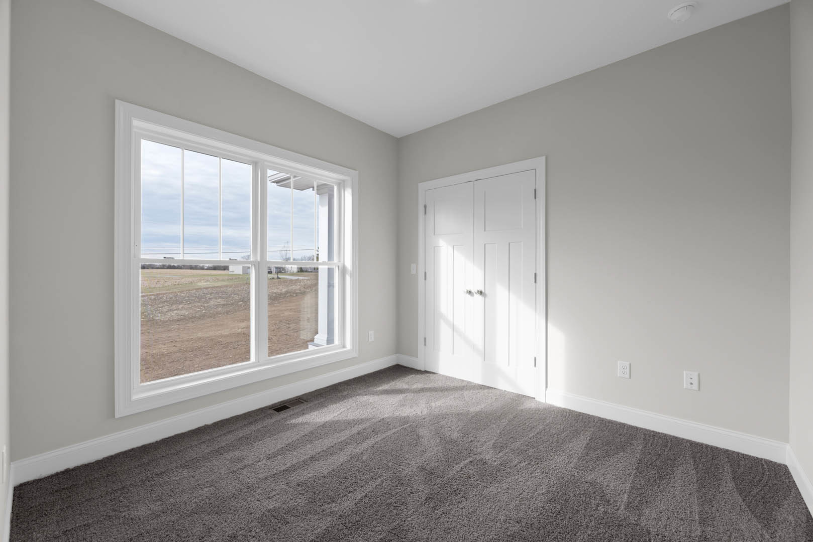 Bedroom with beige carpet, large window overlooking grassy field, white walls, white door with silver knobs, and white ceiling