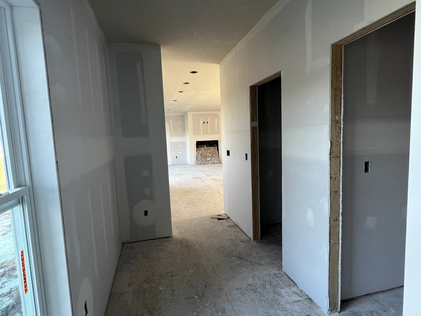 Wide hallway with light grey plaster walls, multiple white doors, wood flooring, and recessed ceiling lights