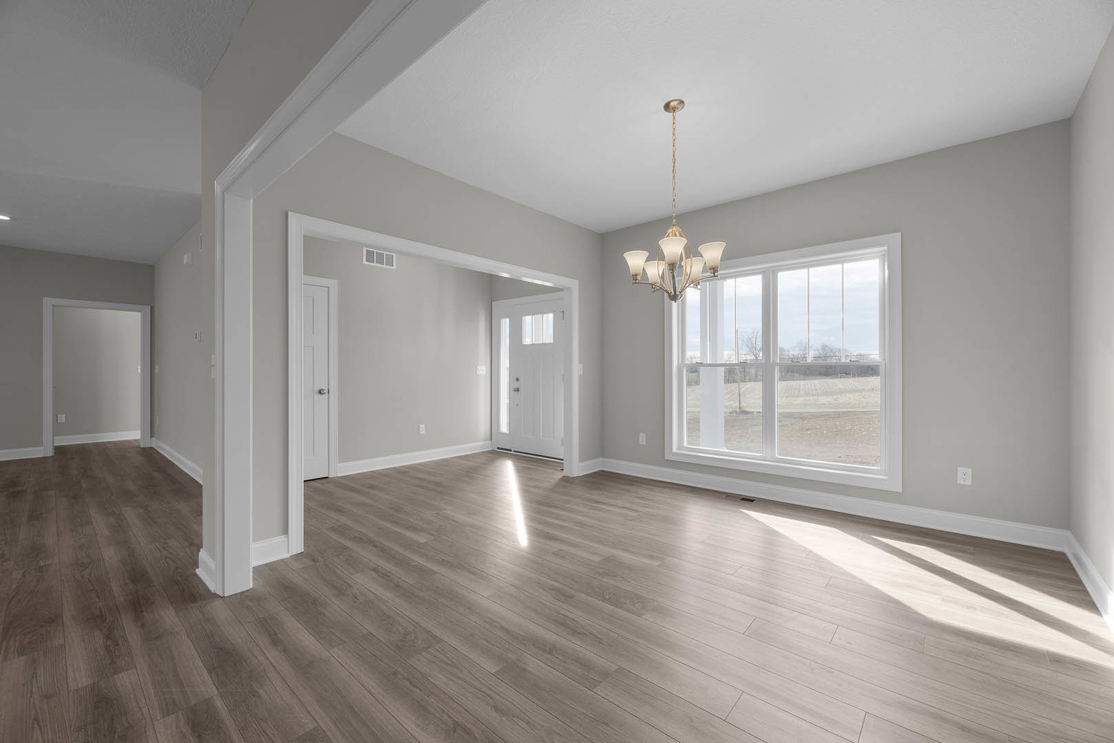 Chandelier hanging from a plaster ceiling above hardwood floors, white framed door with glass panel, large window overlooking grassy field, neutral painted walls