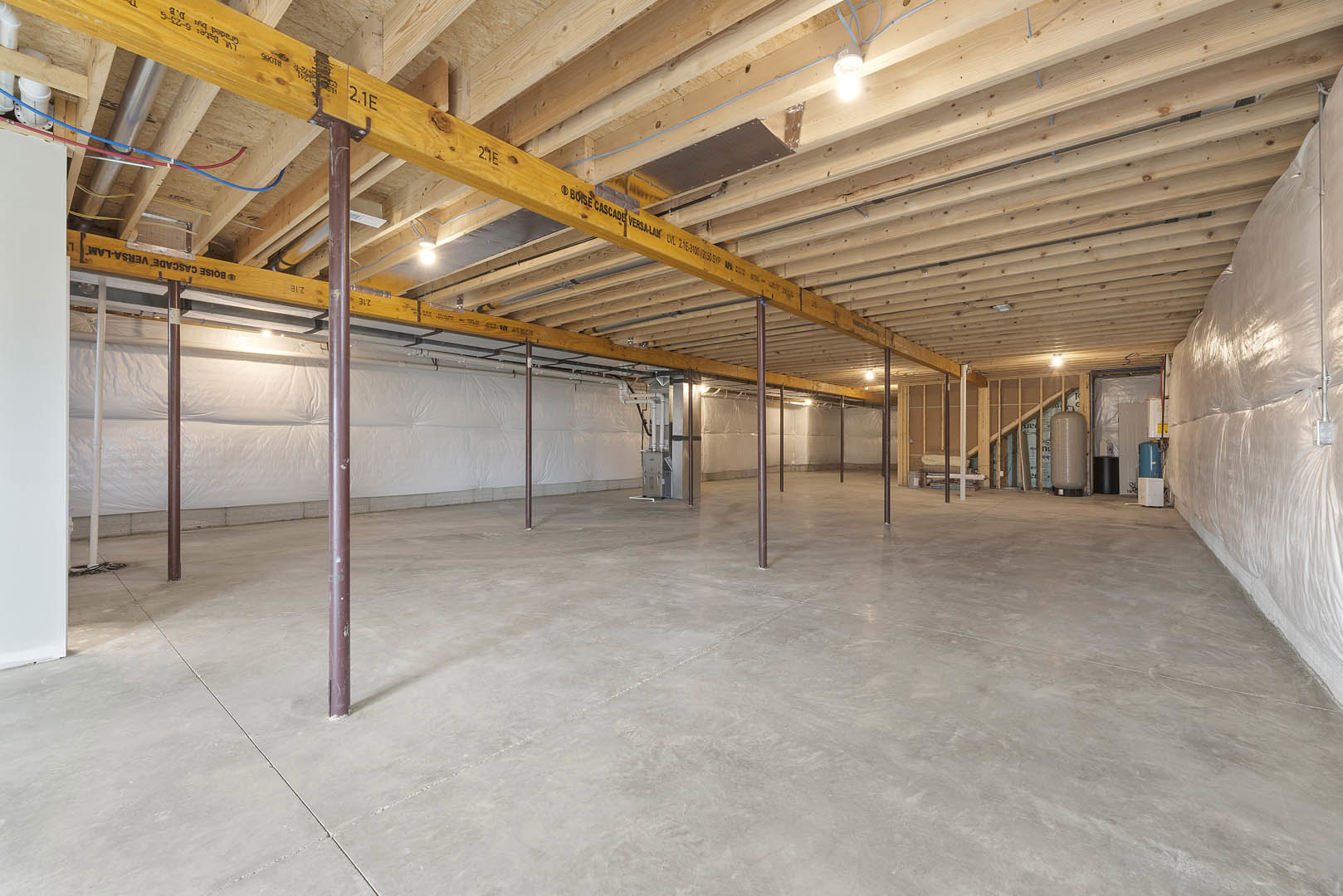 Spacious room with exposed wooden ceiling beams, central metal beam, concrete floor, white walls, and structural poles
