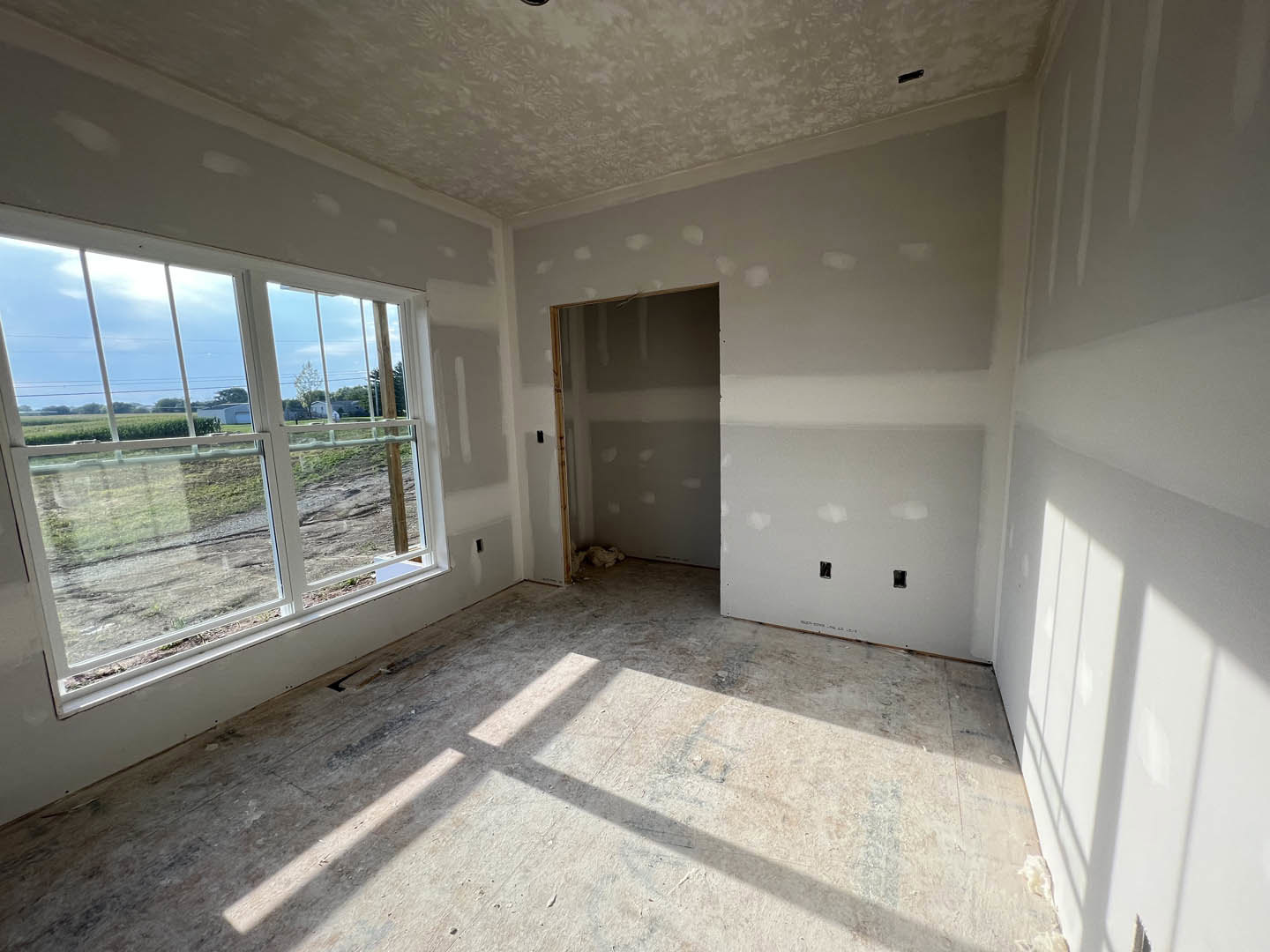 Sunlit room with smooth plaster walls, large window casting shadows on polished concrete floor, white ceiling, and modern door
