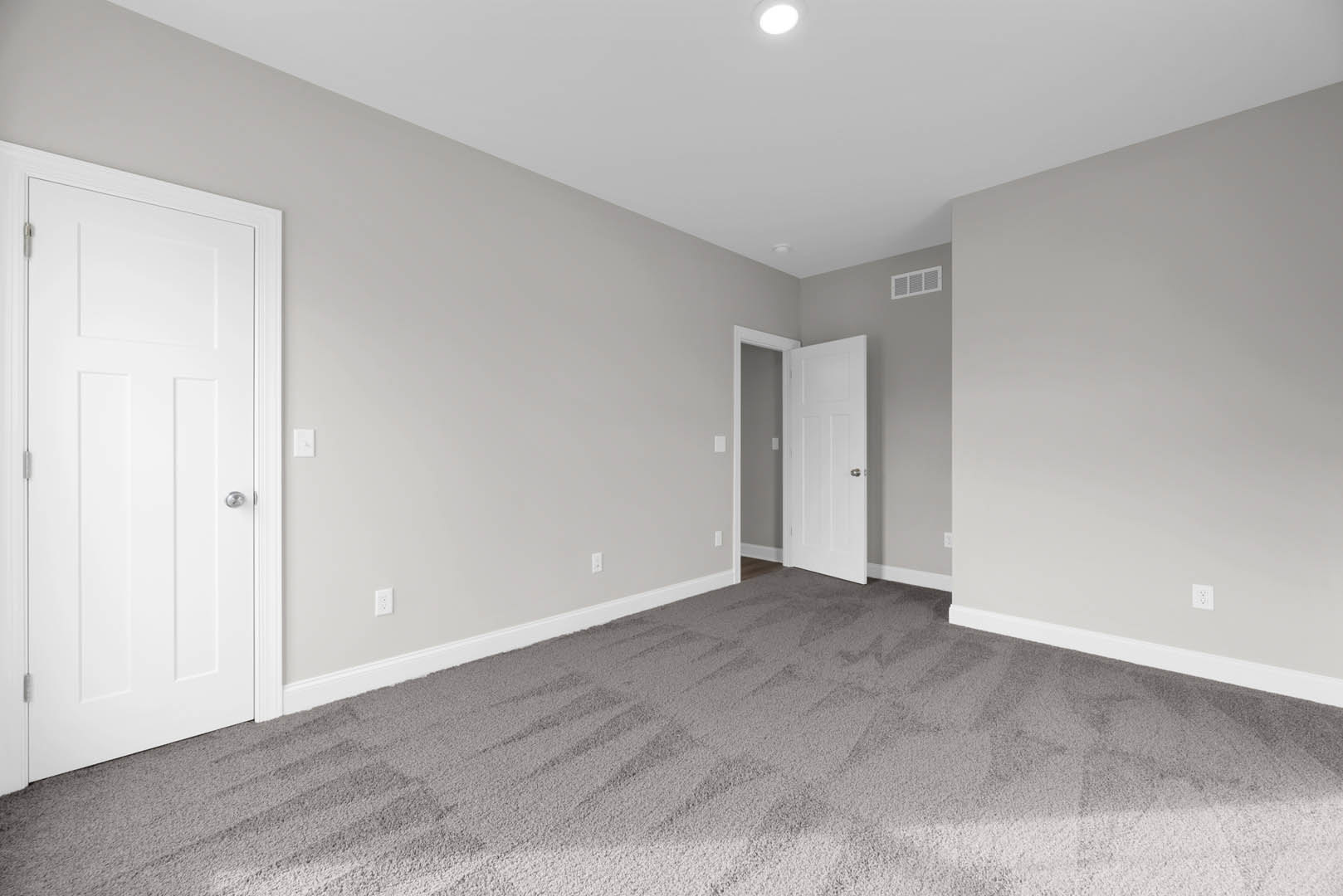 White paneled door with silver knob and adjacent light switch, beige carpet flooring, white walls, and ceiling with exposed light bulb