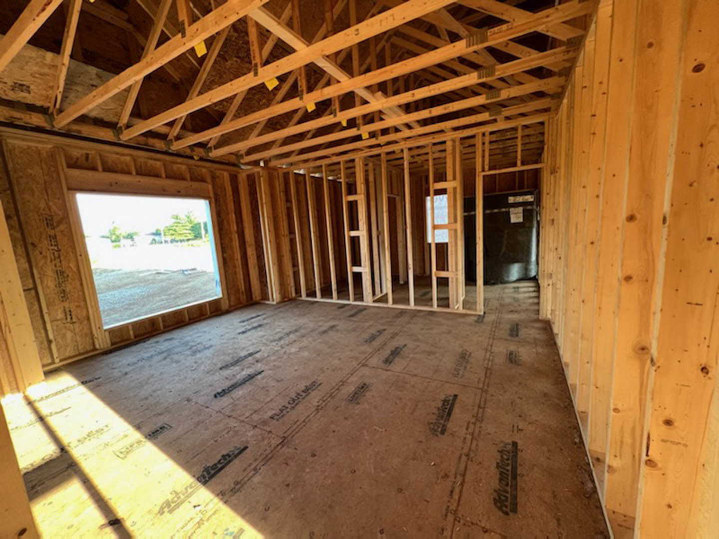 Exposed wood ceiling beams, large window with white trim, unfinished hardwood floor, and visible wall insulation in a residential interior under construction