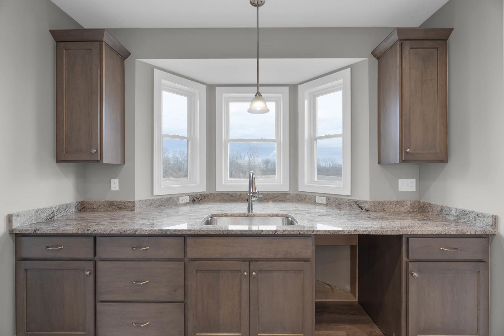 White shaker cabinets and drawers, stainless steel sink with chrome faucet set in quartz countertop, large windows above sink letting in natural light, light gray tile backsplash