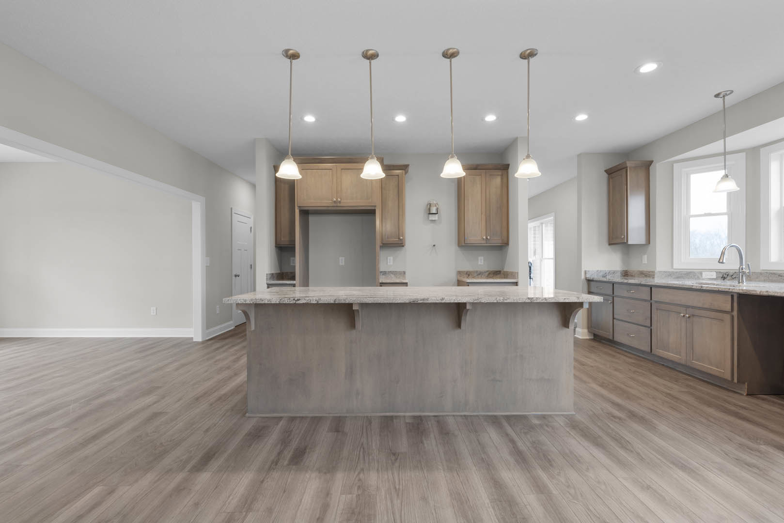 Kitchen with hardwood flooring, central bar counter with shelving, white cabinetry, stone countertops, pendant light fixtures, and neutral wall finishes.