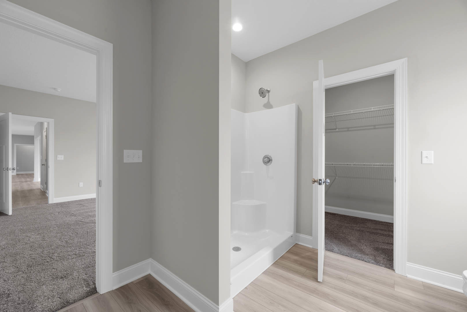 Bathroom with white walls, walk-in shower featuring silver faucet, open door leading to walk-in closet, white wall switch with silver knob, white rectangular thermostat with black