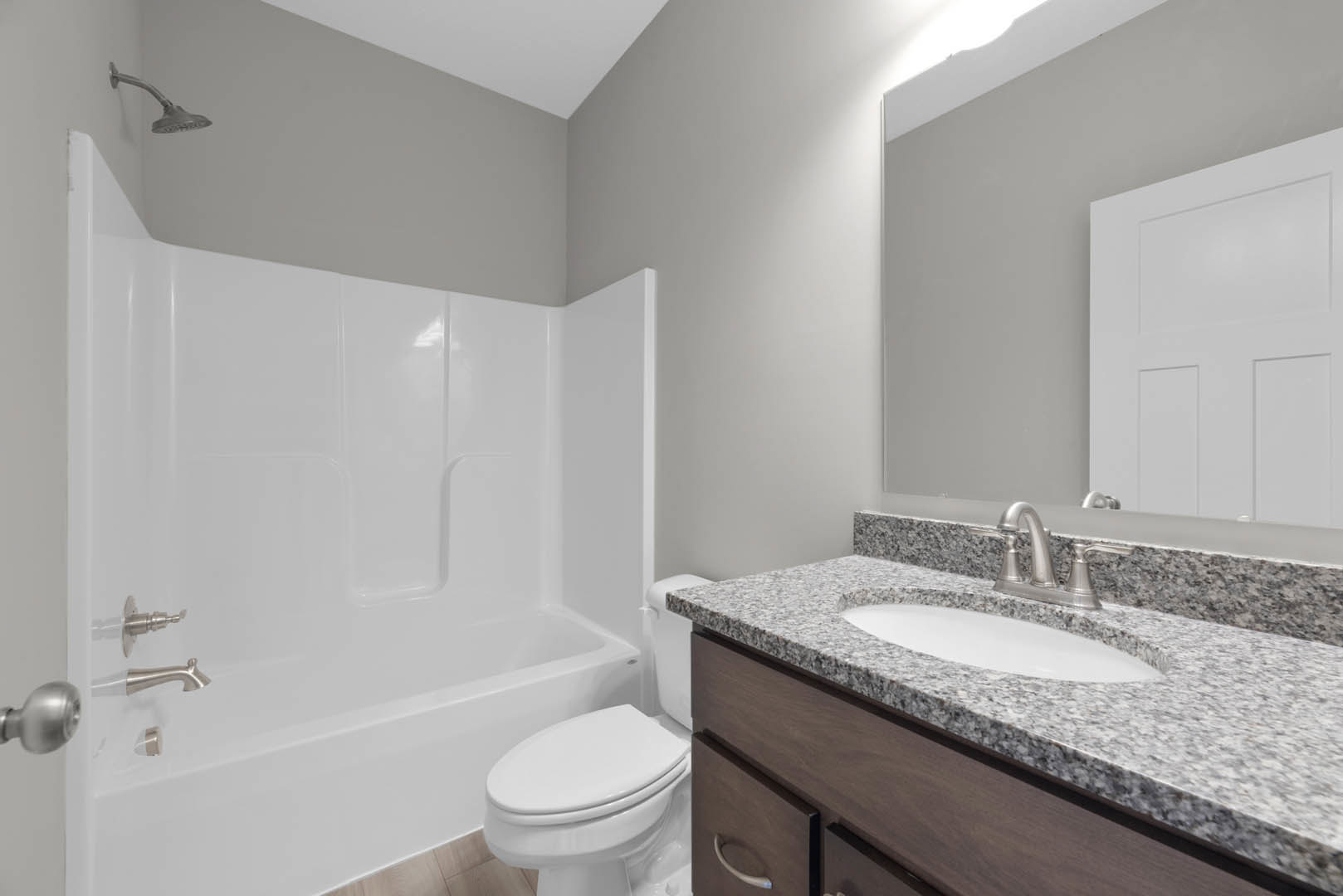 Bathroom with gray countertop vanity, white undermount sink, chrome faucet, freestanding bathtub, white paneled door, wall-mounted shower head, and light tile flooring.