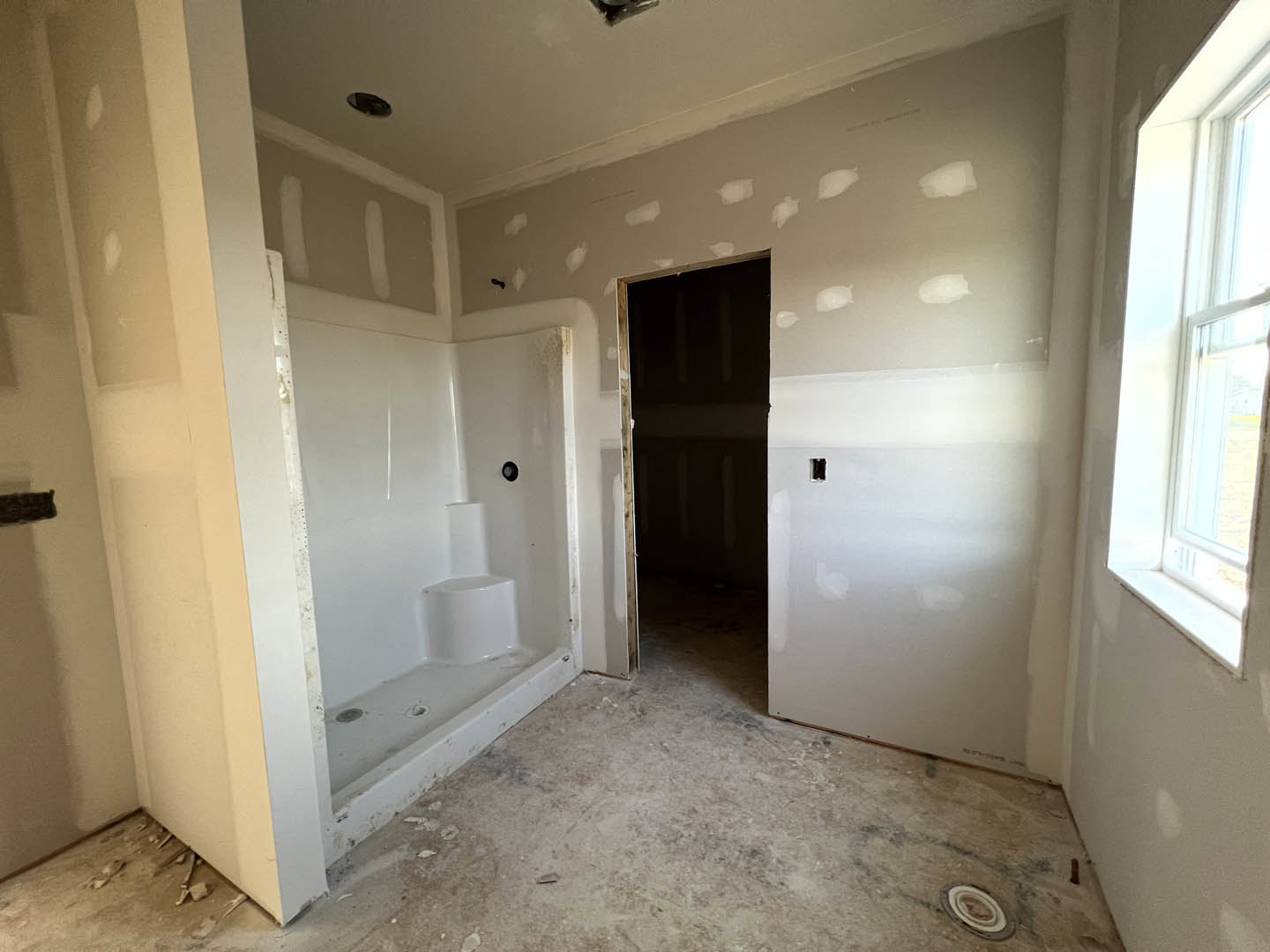 Modern bathroom featuring a glass-enclosed shower, freestanding white bathtub, black door with white trim, light-colored tile flooring, and neutral plaster walls.