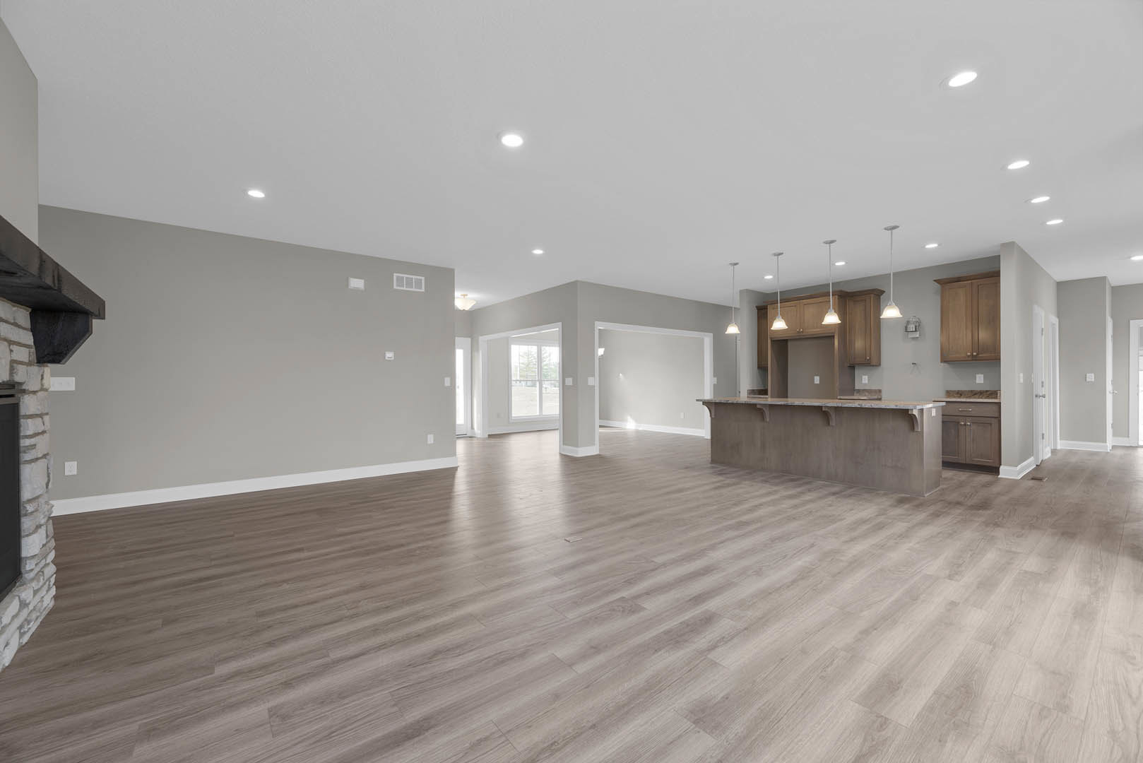 Spacious open floor plan featuring wood flooring, white walls, large windows, marble kitchen countertop, white ceiling with recessed lighting, and sleek cabinetry