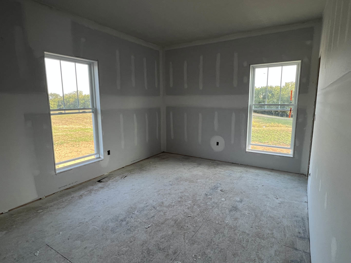 Spacious room featuring large windows, polished concrete floor, plaster walls, and views of grassy field and trees