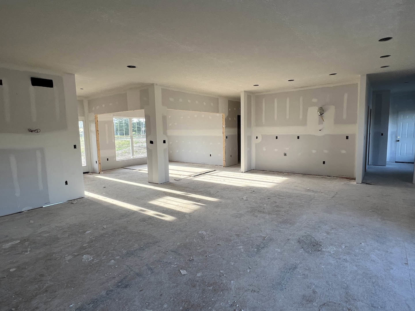 White-walled room featuring a large window, white pillars, and a white door with a black handle; light-colored flooring and plaster ceiling visible.