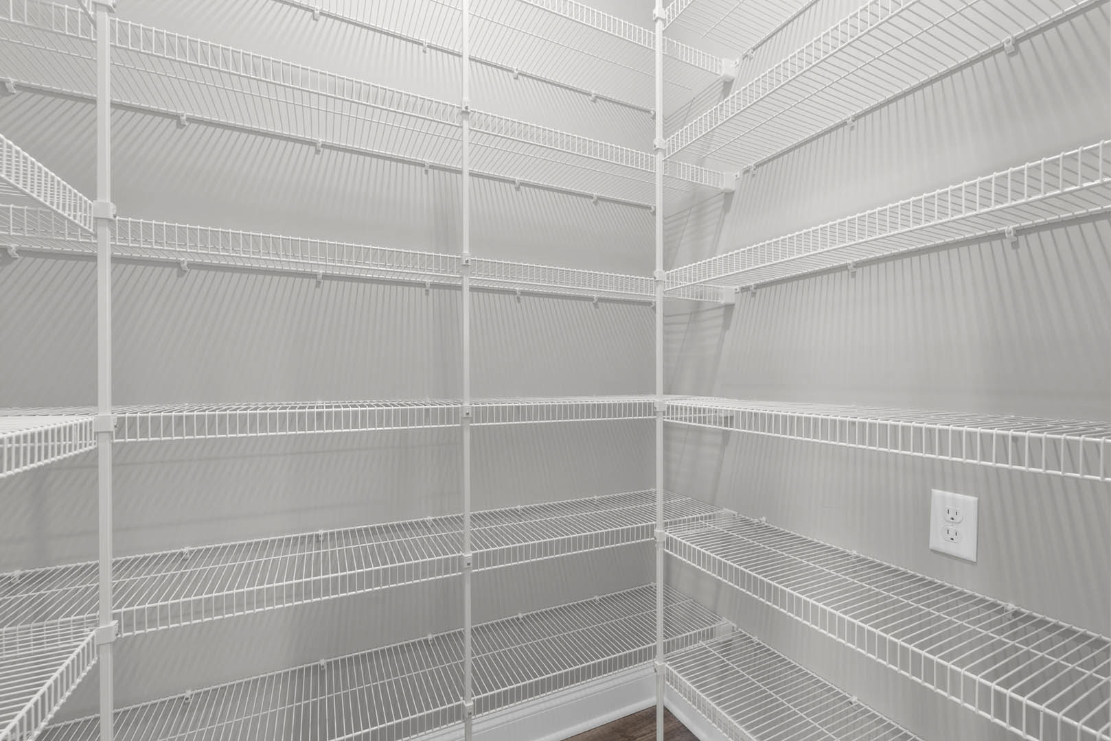 White closet with wire shelving, empty interior, white walls, and visible wall outlet