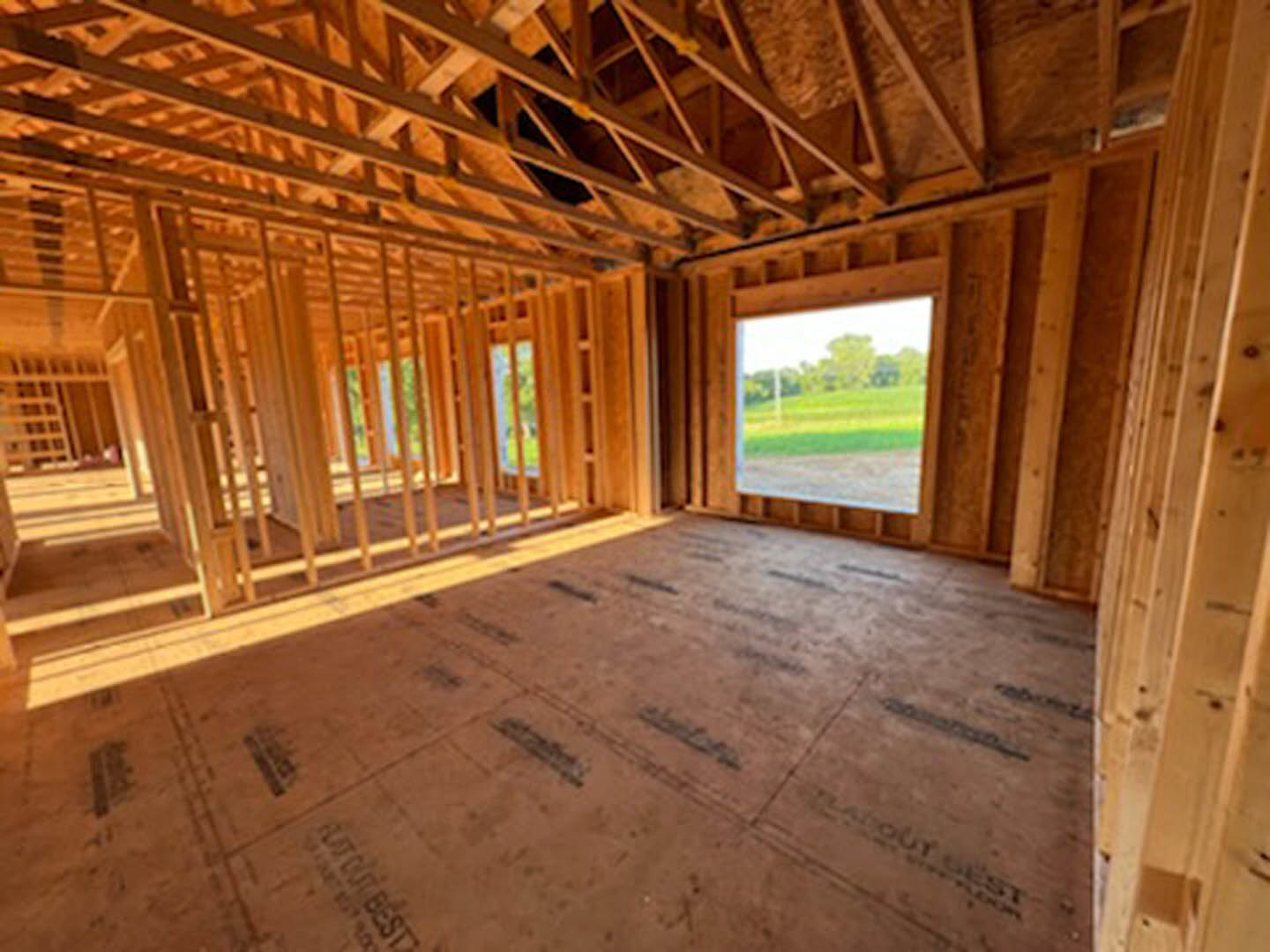 Living room with exposed wood ceiling beams, hardwood flooring, large window overlooking grassy field and trees