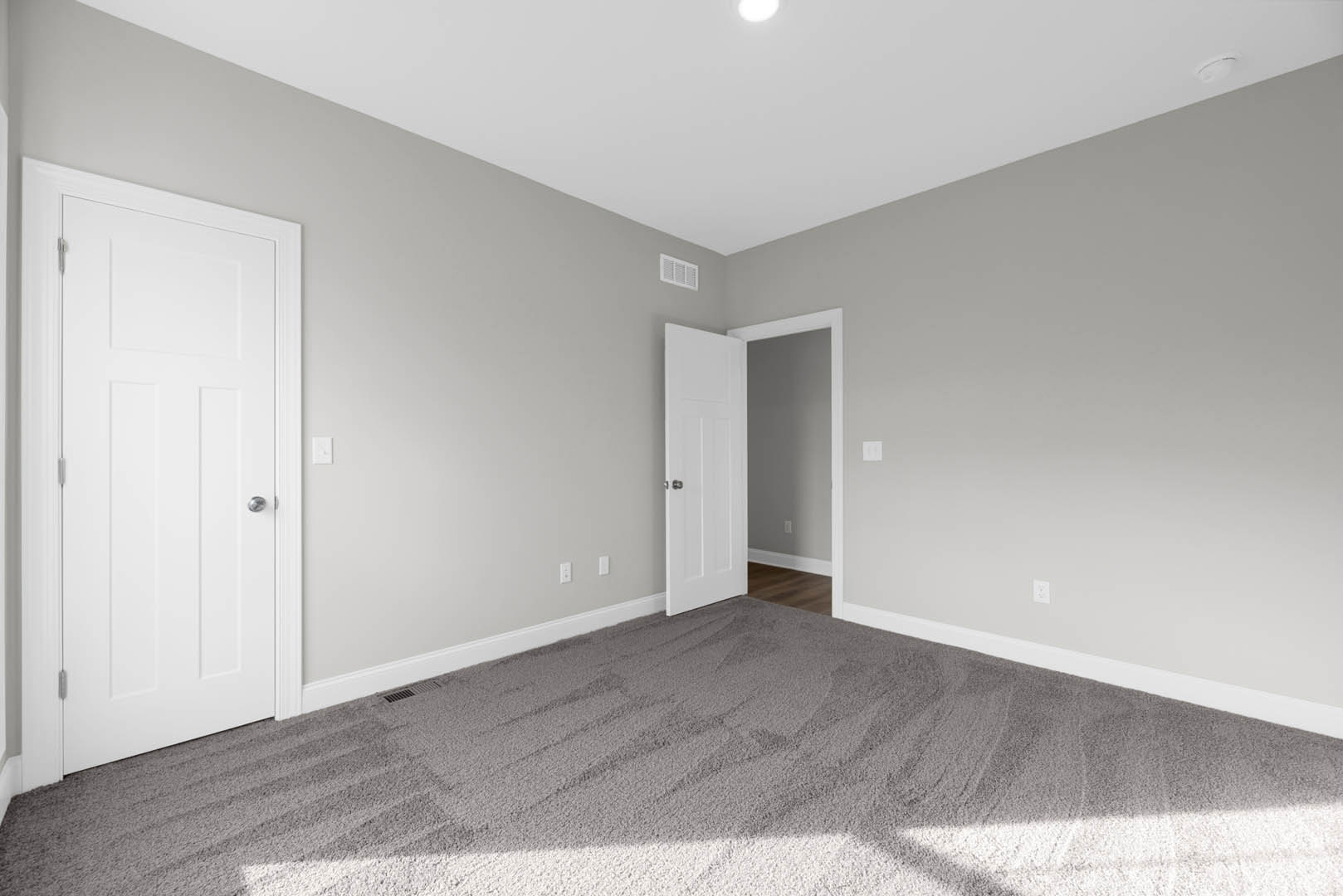White paneled door with silver knob, beige carpeted floor, white wall vent, and circular wall plate in a neutral room with plaster walls and ceiling.