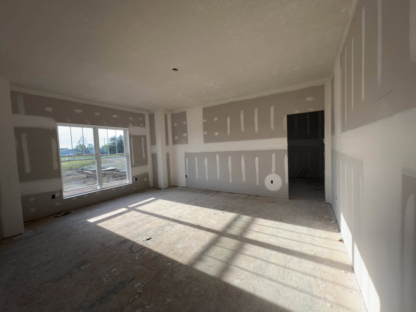 Bright room with smooth white plaster walls, large window overlooking dirt field, light-colored flooring, and simple ceiling detailing
