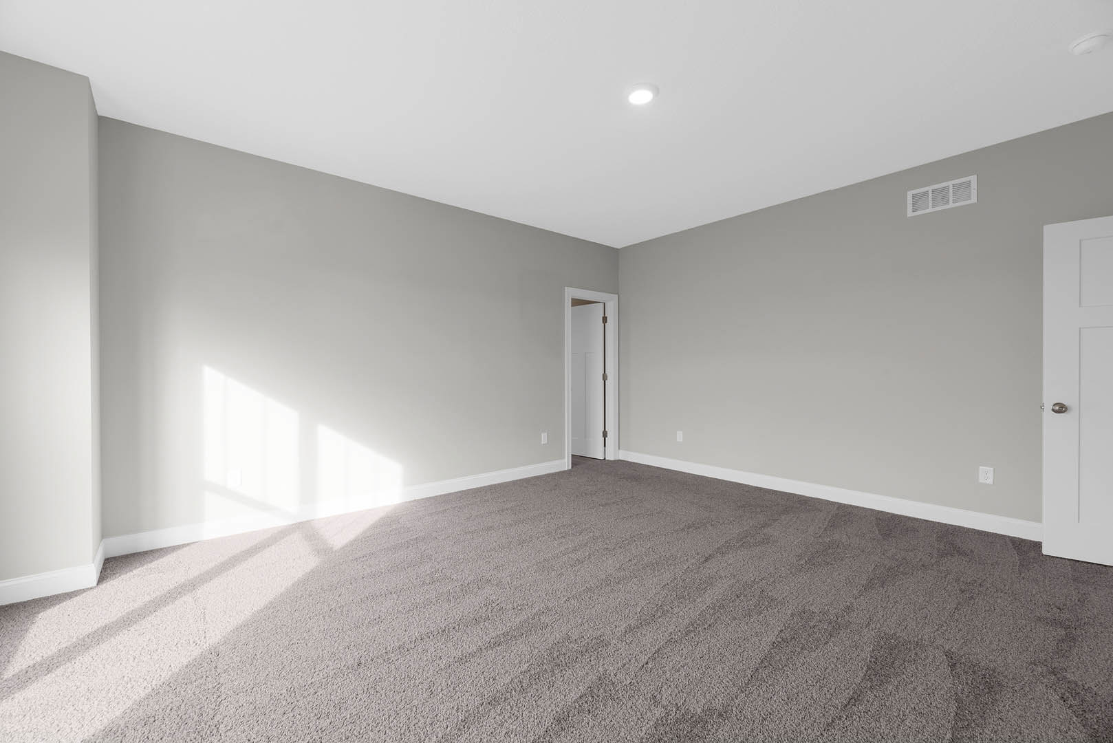 White paneled door with brushed metal handle open to carpeted room, white plaster walls, ceiling vent, and recessed lighting