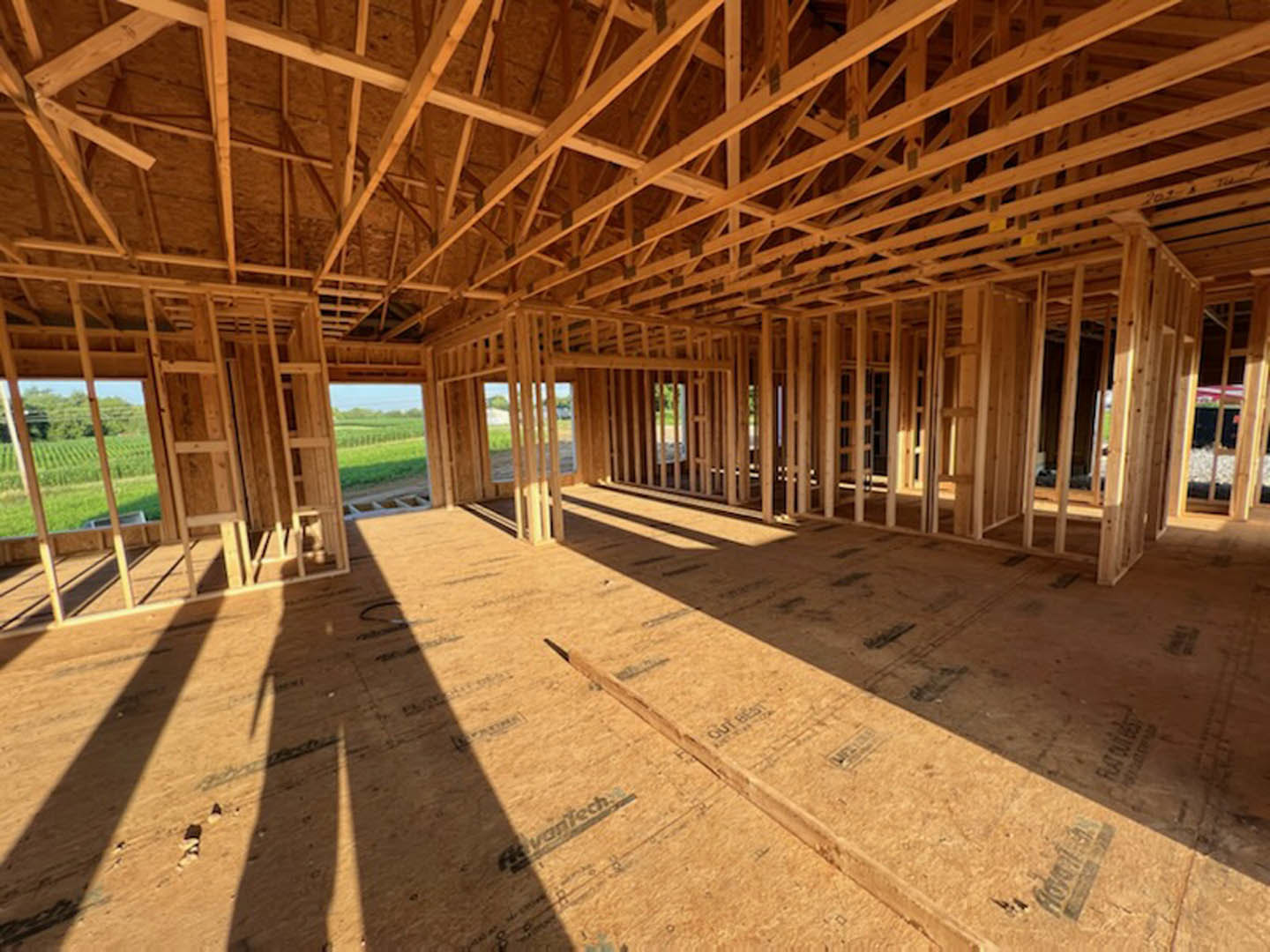 Wood-framed house under construction on grassy field, exposed beams and unfinished roof structure visible