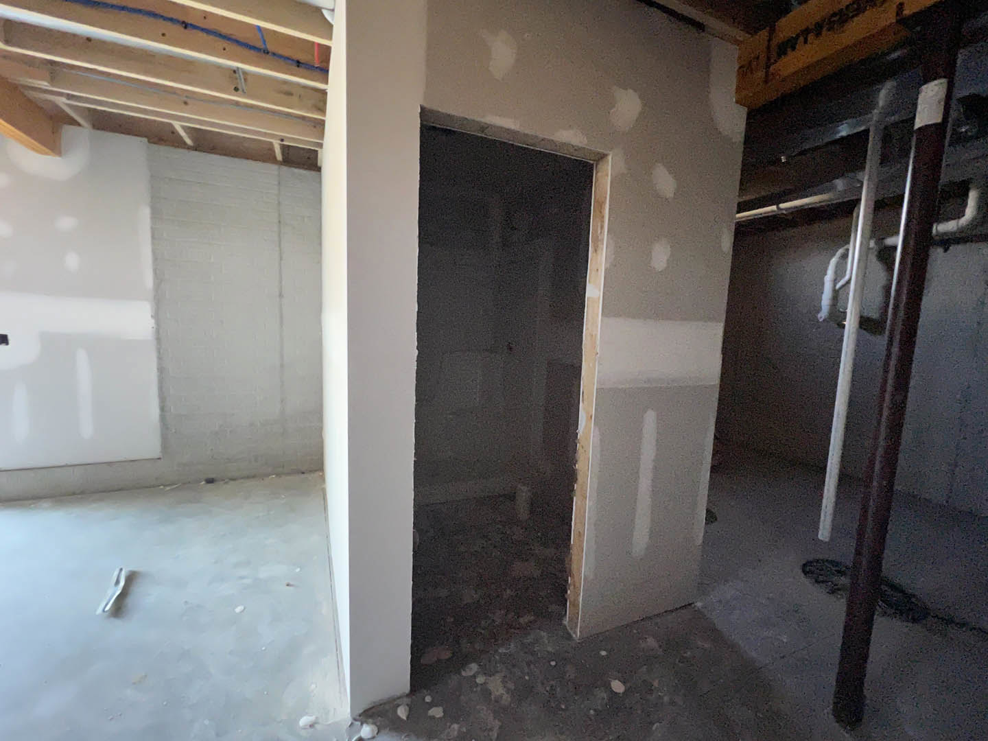 White plaster wall with black fixture, wooden ceiling beams, closed door, and light-colored floor in a custom home interior.