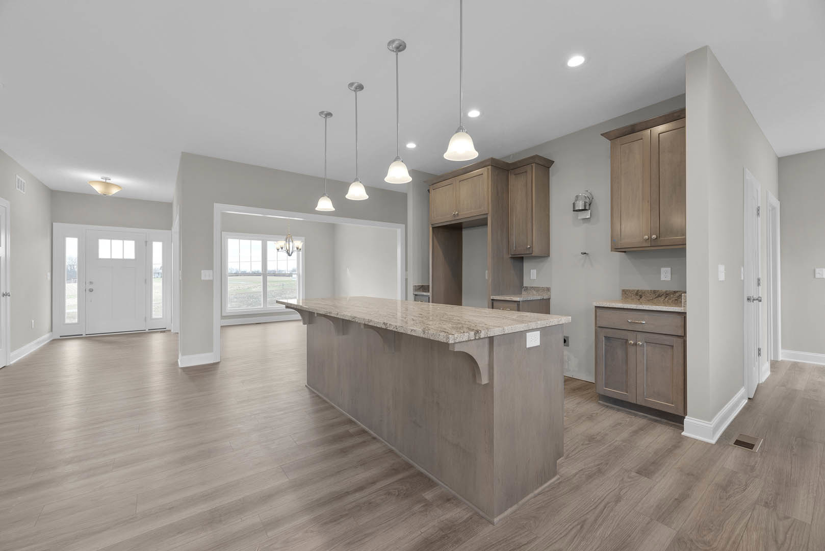 Spacious kitchen featuring a large central island with stone countertop, white cabinetry, stainless steel sink, and a white door with glass panes; light wood flooring and recessed