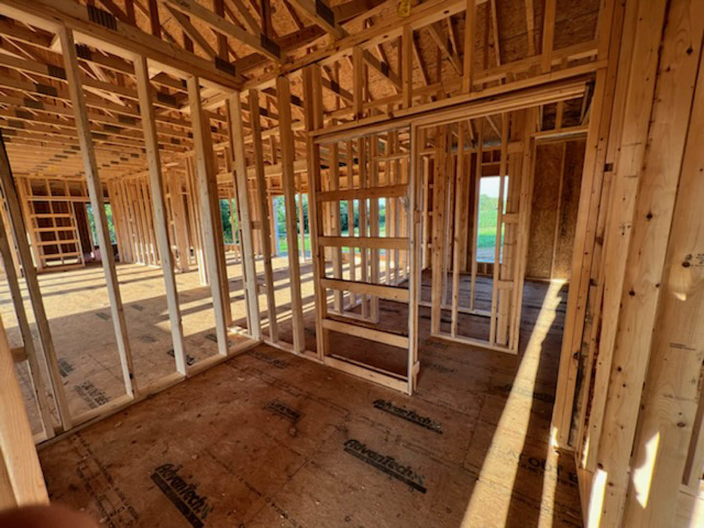 Wood framing and exposed beams inside a house under construction, unfinished floors and ceiling, natural daylight illuminating lumber and planks