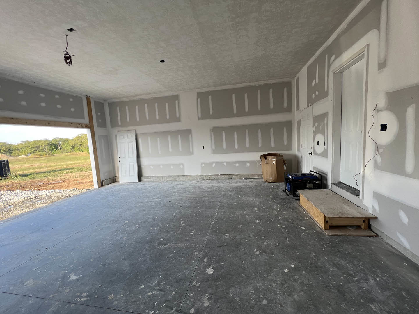 White door with black knobs set in a room featuring grey flooring, a wooden box, a brown bag with a broken top, and a blue and black generator.