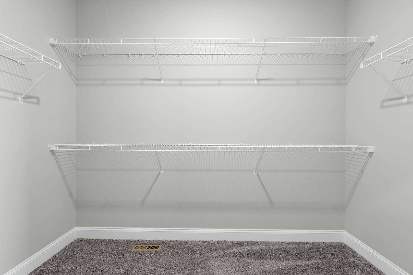 White wire shelving mounted on plaster walls above beige carpet in an empty room