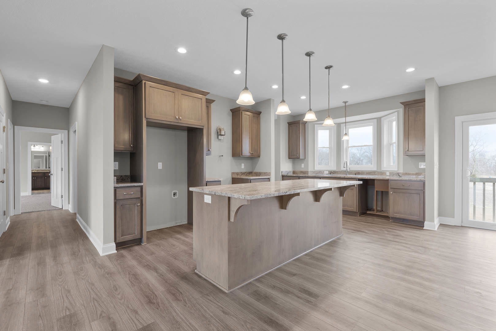 Spacious kitchen featuring a marble-topped island, white cabinetry, stainless steel sink, laminate flooring, and modern pendant lighting.