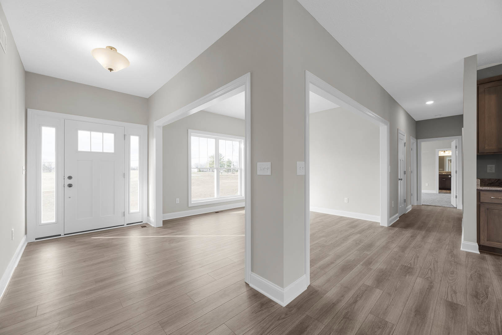 White walls and wood flooring in a bright room, featuring a white door with glass panes, a window overlooking a field, and a modern light fixture.