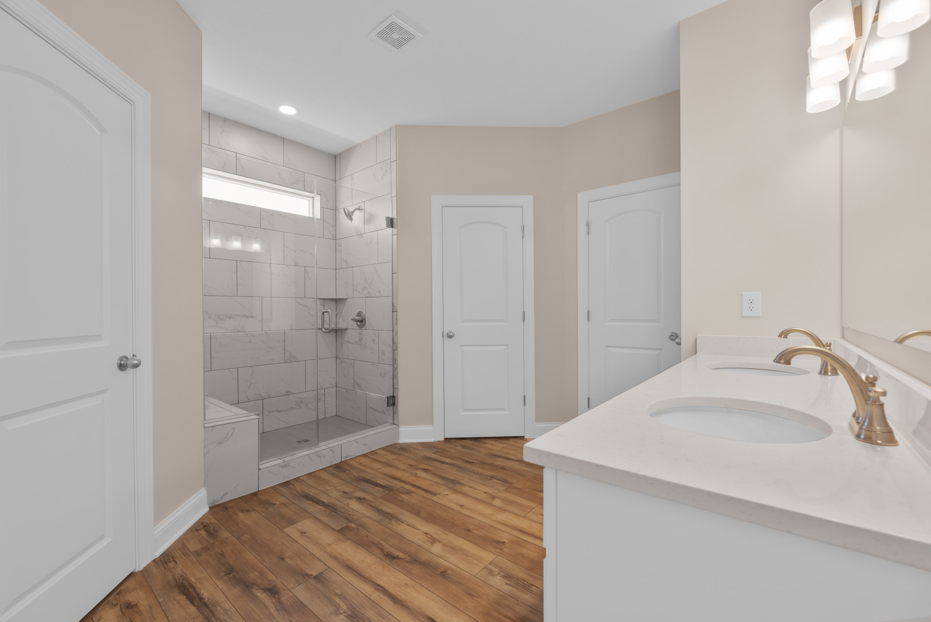 Bathroom with white tile shower, white sink and chrome faucet, white door with silver knob, modern light fixture, neutral walls and flooring