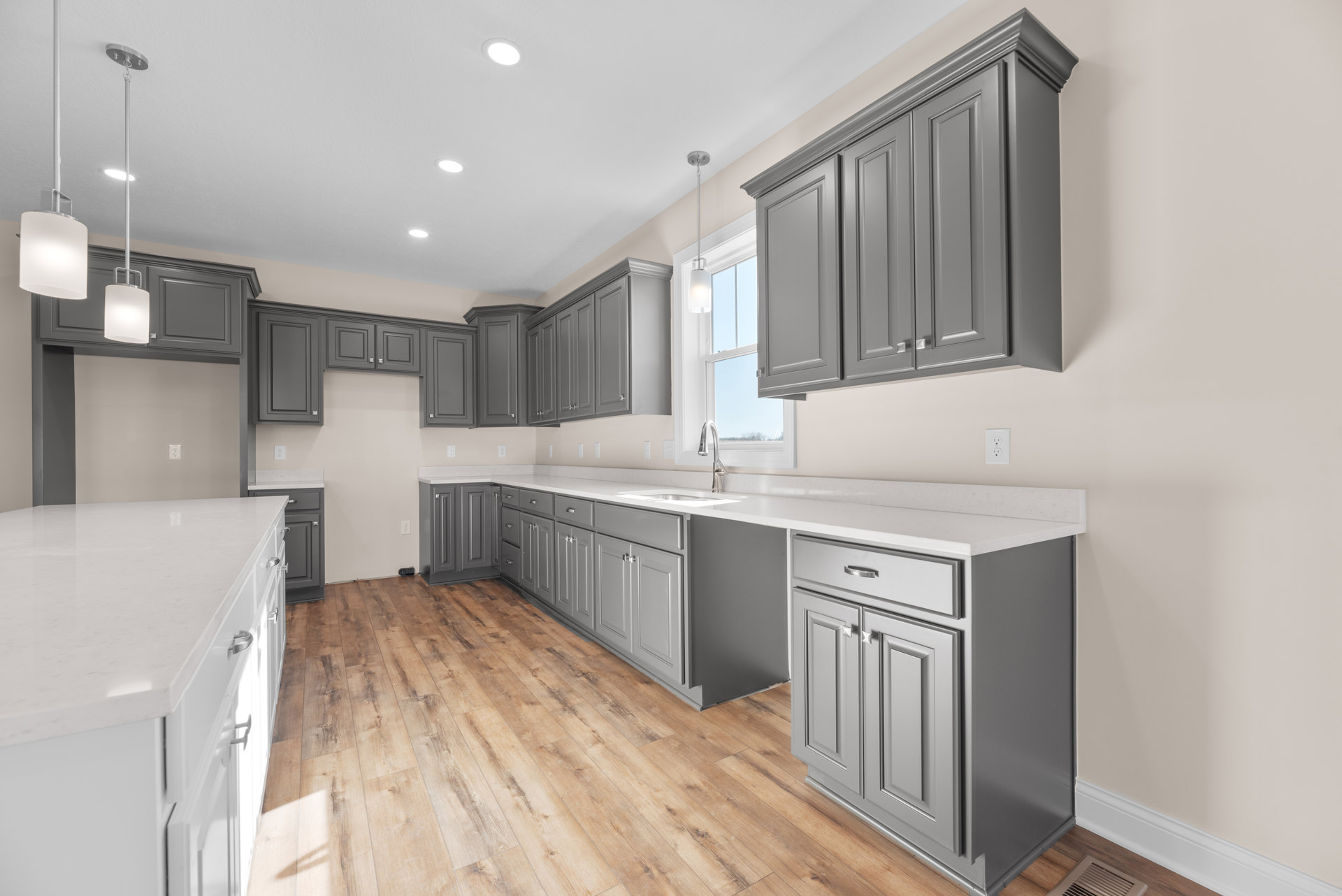 Grey kitchen cabinets with white countertops, wood flooring, and stainless steel appliances