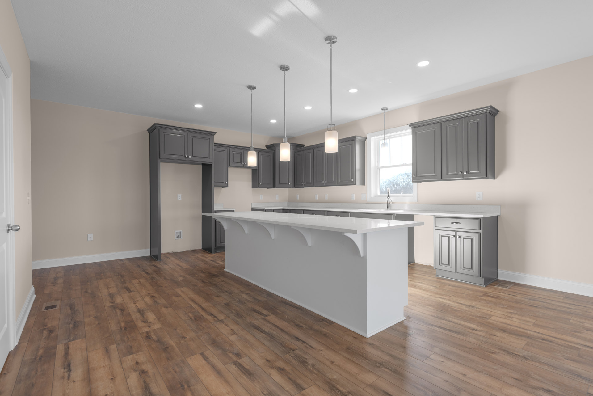 Spacious kitchen featuring a large white island with waterfall countertop, light wood flooring, grey cabinetry, stainless steel sink, and white paneled doors